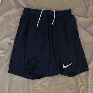  träningsshorts Nike - Säljer ett par svarta träningsshorts från Nike med vit snörning i midjan och en vit Nike-logga på benet. Perfekta för sport och träning.