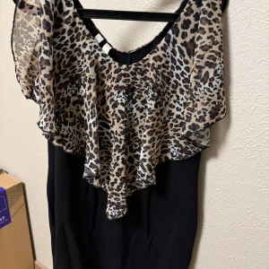 Leopardmönstrad klänning från Bodyflirt - Snygg klänning från Bodyflirt med leopardmönstrad överdel och svart underdel. Den har en volangdetalj som ger en extra touch. Perfekt för dig som vill sticka ut med ett djärvt mönster.