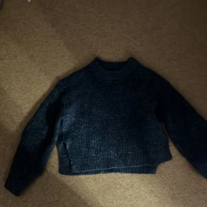 Mörkgrå stickad tröja från Gina Tricot - Säljer en mysig mörkgrå stickad tröja från Gina Tricot. Tröjan har en croppad design med långa ärmar och ribbade detaljer vid ärmslut och nederkant. Perfekt för kyliga dagar!