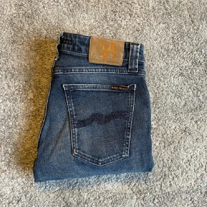 Mörkblå jeans från Nudie - Snygga mörkblå jeans från Nudie med en klassisk femficksdesign. De har en slim passform och är tillverkade i högkvalitativt denim. Perfekta för en stilren look. Storlek W29 L32 och modell skinny lin. Vid fråga eller fundering hör av dig. Mvh Levi!