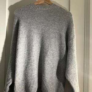 Grå stickad tröja - Mysig grå stickad tröja med ribbade detaljer vid hals och nederkant. Perfekt för kyliga dagar och ger en avslappnad look. Passar bra till jeans eller leggings.