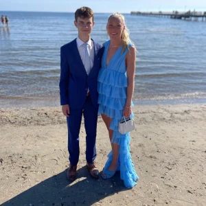 Blå volangklänning/balklänning - Säljer en fantastisk blå långklänning med volanger och djup v-ringning. Klänningen har en asymmetrisk design med flera lager av volanger som ger en härlig rörelse. Perfekt för sommarens festligheter! 💙 endast använd på balen. Det är storlek 38 men vi har sytt in en resår i midjan så den passar xs/s, men den går såklart att ta bort. Det är Hannah schönberg x nakd