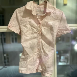 Ljusrosa kortärmad skjorta - Säljer en ljusrosa kortärmad skjorta med knappar framtill. Perfekt för varmare dagar och har en klassisk krage. Knappt använd.