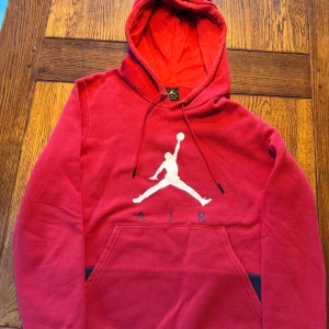 Röd hoodie från Air Jordan - Säljer en snygg röd hoodie från Air Jordan med den ikoniska Jumpman-loggan i vitt på framsidan. Hoodien har en praktisk känguruficka och justerbar huva med dragsko. Perfekt för en sportig look eller avslappnade dagar.