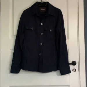 Mörkblå overshirt från Oscar Jacobson - Säljer en stilren mörkblå overshirt från Oscar Jacobson. Den har långa ärmar och knappar framtill, perfekt för lager-på-lager under hösten. Två bröstfickor med knappar ger en snygg detalj. Passar både till vardags och lite finare tillfällen. 