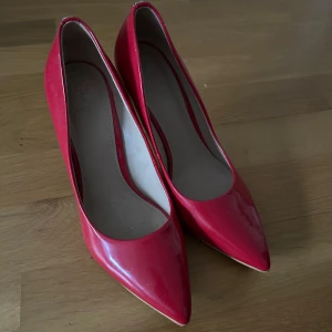 Röda klackskor från Guess - Säljer ett par snygga röda klackskor från Guess. De har en spetsig tå och en elegant klack. Perfekta för fest eller en utekväll! Skorna är i bra skick och har en stilren design.