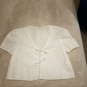 Blus - Vit blus med två söta rosetter där fram. Jättefint skicka man kan knappt se att den har används. 