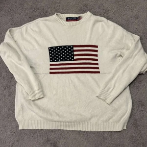 Vit stickad tröja med amerikansk flagga - Säljer en vit stickad tröja från Focus med en stor amerikansk flagga på framsidan. Tröjan har långa ärmar och ribbstickade muddar vid ärmslut och nederkant. Perfekt för en avslappnad stil. Hör av er med frågor!