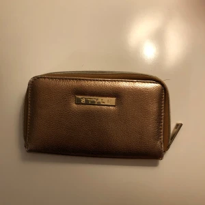 Guldig plånbok med dragkedja - Snygg guldig plånbok med dragkedja och flera fack för kort och kontanter. Perfekt för att hålla ordning på dina tillhörigheter med stil. Märket 'STYLE' pryder framsidan.