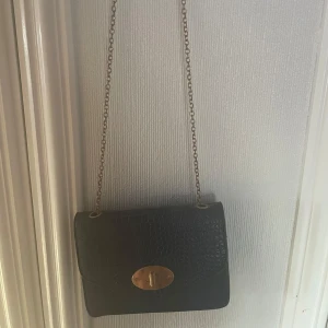 Svart axelväska med kedja - Snygg marinblå/mörkblå axelväska med kedja och elegant låsdetalj framtill. Väskan har en stilren design med en struktur som ger den en lyxig känsla. Perfekt för att lyfta vilken outfit som helst. 