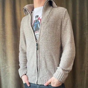 Grå stickad kofta - Säljer en stilren grå stickad kofta med dragkedja och ribbad krage. Koftan har långa ärmar med förstärkta armbågar i mörkare tyg och ribbade muddar. Perfekt för kyliga dagar! Vid minsta fråga eller fundering hör av er🤝