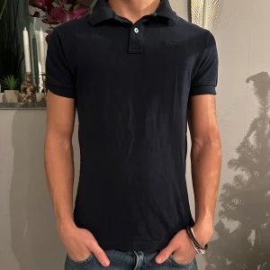 Marinblå pikétröja - Snygg svart pikétröja med krage och korta ärmar. Perfekt för en stilren och avslappnad look. Passar bra till jeans eller chinos.