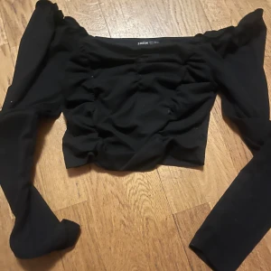 Svart offshoulder topp från Shein - Trendig svart offshoulder topp från Shein med långa ärmar. Perfekt för en stilren look. Toppen har en åtsittande passform och är tillverkad i ett mjukt material.