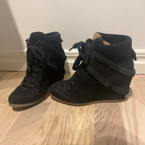 Svarta sneakers med kilklack - Snygga svarta sneakers med kilklack och snörning. Skorna har en stilren design med en högre ankel och är tillverkade i mocka. Perfekta för en trendig look.