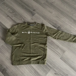 Olivgrön tröja från Sail Racing - Säljer en olivgrön tröja från Sail Racing med långärmad design. Lite sprucket tryck 