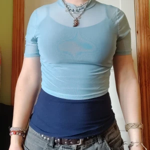 Ljusblå mesh polotopp - Snygg ljusblå mesh polotopp med korta ärmar. Perfekt för lager-på-lager-stil eller som statement-plagg. Toppen är inte mönstrad som på andra bilden det är ljuset som spökar utan enkel transparent topp som är tight i passformen.