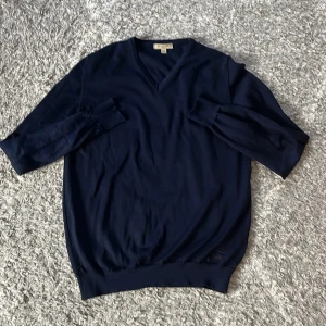 Mörkblå tröja från Burberry - Snygg mörkblå tröja från Burberry med en broderad logga. Perfekt för en stilren look. Har två lagade hål som knappast syns. Den är äkta och är i 100% merinoull. Ny pris ca 7000. Hör av er vid frågor eller prisförslag.