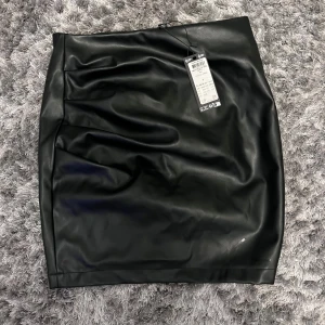 Svart kjol från Vero Moda - Snygg svart kjol i skinnimitation från Vero Moda. Aldrig använd & säljer då den aldrig kommit till användning, prislappen är kvar. Finns ej bild på hur den ser ut på❣️
