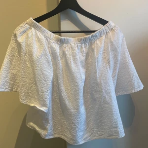 Vit offshoulder topp - Säljer en luftig vit offshoulder topp med textur. Perfekt för varma sommardagar. Den har en elastisk kant som håller toppen på plats och ger en avslappnad look.
