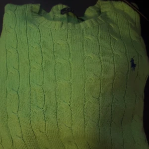 Grön stickad tröja från Ralph Lauren - Cable-Knit Cotton Jumper.    Säljer en snygg grön stickad tröja från Ralph Lauren med kabelstickat mönster. Tröjan har en klassisk rund halsringning och den ikoniska loggan broderad på bröstet. Perfekt för en stilren look!