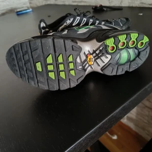 Svarta Nike sneakers med gröna detaljer - Snygga svarta Nike sneakers med unika gröna detaljer och vågformade mönster. Skorna har en robust sula med bra grepp och klassisk snörning. Perfekta för en sportig look.