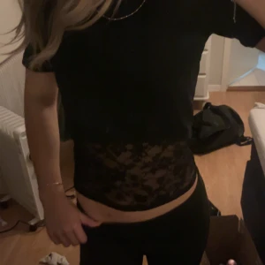 Svart kortärmad topp med spetsdetaljer - Snygg svart topp med korta ärmar och spetsdetaljer i midjan. Perfekt för en trendig look med en touch av elegans.