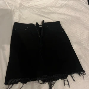 Svart jeanskjol från NA-KD - Snygg svart jeanskjol från NA-KD med fransig nederkant. Perfekt för en trendig look.