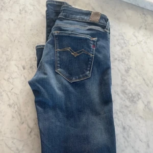 Blå jeans från Replay - Snygga blå jeans från Replay med klassisk femficksdesign och subtila slitningar. De har en knappgylf och märkesdetaljer på fickorna. Perfekta för en avslappnad stil.