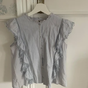 Ljusblå blus med spetsdetaljer, Zadig  - Charmig ljusblå blus med spetsdetaljer och volanger längs ärmarna. Blusen är ärmlös och har en knäppning framtill. Perfekt för en somrig look. Från Zadig