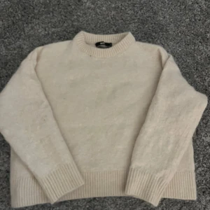 Beige stickad tröja från Bik Bok - Mysig beige stickad tröja från Bik Bok i alpackablandning. Tröjan har en klassisk rund hals och ribbade muddar vid ärmslut och nederkant. Perfekt för kyliga dagar.