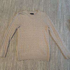 Beige stickad tröja från Bondelid - Säljer en stilren beige stickad tröja från Bondelid. Tröjan har ett klassiskt kabelstickat mönster och långa ärmar. Perfekt för kyligare dagar.