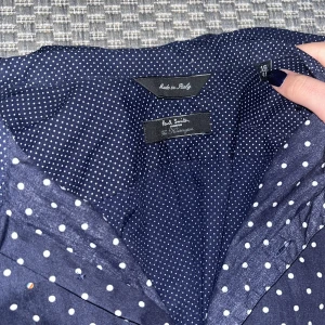 Mörkblå prickig skjorta från Paul Smith - Snygg mörkblå skjorta från Paul Smith med vita prickar. Tillverkad i Italien, perfekt för en stilren look. Skjortan har långa ärmar och knappar framtill. Ett klassiskt val för den modemedvetna.