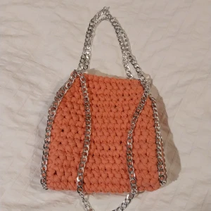 Rosa virkad väska med kedjor - Trendig rosa virkad väska med silverfärgade kedjehandtag. Perfekt för att ge din outfit en unik touch. Den stickade designen ger en mysig känsla och kedjorna tillför en cool detalj.