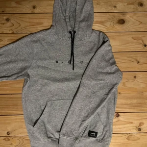 Grå hoodie från !Solid - Säljer en stilren grå hoodie från !Solid med trycket 'A.R.C.' på bröstet. Tröjan har en praktisk magficka och justerbar huva med svarta snören. Perfekt för en avslappnad look. Knappt använd.
