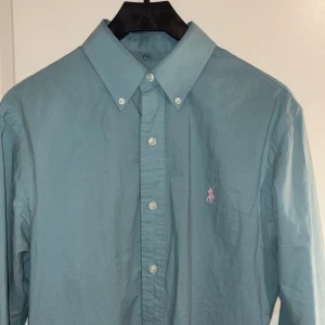 Grön skjorta från Ralph Lauren - Snygg grön skjorta från Ralph Lauren i slim fit. Tillverkad i 100% bomull. Den har en broderad rosa logotyp på bröstet som ger en stilren touch. Priset är diskuterbart:)