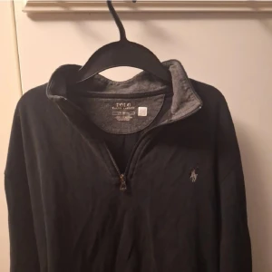 Svart tröja med dragkedja från Polo Ralph Lauren - Snygg svart tröja från Polo Ralph Lauren med halv dragkedja och broderad logga på bröstet. Perfekt för en stilren och avslappnad look.