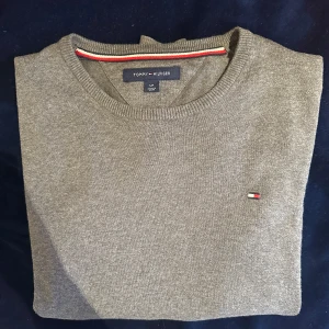 Grå tröja från Tommy Hilfiger - Säljer en stilren grå tröja från Tommy Hilfiger i storlek s. Tröjan har en rund halsringning och det klassiska Hilfiger-emblemet på bröstet. Perfekt för en avslappnad och snygg look. Tröjan är i mycket bra sick utan defekter. 
