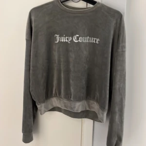 Grå velourtröja från Juicy Couture - Säljer en mjuk och stilren grå velourtröja från Juicy Couture med glittrande logotyp på framsidan. Tröjan har långa ärmar och en avslappnad passform, perfekt för en bekväm och trendig look.