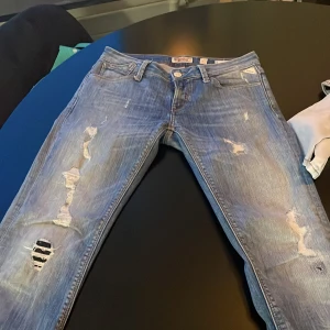 Blå jeans från Replay - Snygga blå jeans från Replay med slitna detaljer och broderad logga på baksidan, storlek är W27 L32