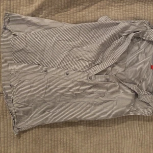 Randig topp - Säljer en stilren randig ärmlös topp i blått och vitt med knappar framtill. Perfekt för en avslappnad men ändå snygg look. 