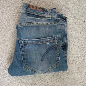 Dondup jeans - Snygga blå jeans med raka ben och klassisk femficksdesign. De har en diskret tvättad look och orange detaljer vid midjan. Perfekta för en avslappnad stil. Jeansen med märke dondup kostar 3000 nya, säljer eftersom dom inte passar mig