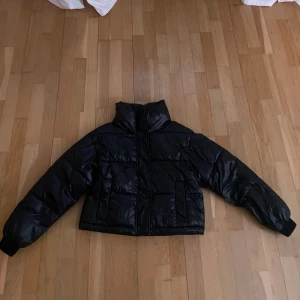 Svart pufferjacka - Snygg svart pufferjacka med dragkedja och hög krage. Perfekt för kyliga dagar med sin vadderade design som håller dig varm. Jackan har långa ärmar och en stilren look.