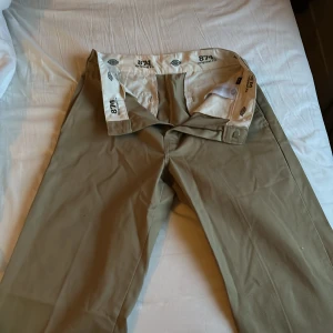 Beige byxor från Dickies - Säljer ett par klassiska beige byxor från Dickies. De har en rak passform och är tillverkade i slitstarkt material. Perfekta för en avslappnad stil. Byxorna har knappar och hällor för bälte.