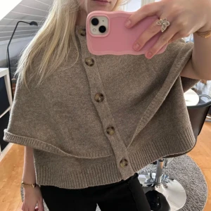  Zara tröja - Säljer en stilren beige stickad cape från Zara med knappar framtill. Perfekt för lager-på-lager och ger en elegant touch till din outfit. Den har en rund hals och ribbade kanter. Ny pris 550 kr