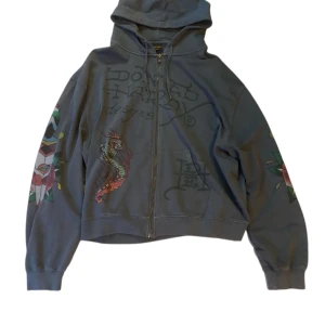 Ed Hardy hoodie - Säljer en grå/mörkblå Ed hardy zip up hoodie som är sjukt snygg med flera feta tryck runt om tröjan. . Hoodien har en bekväm och oversized passform. Den är typ aldrig använd och har inga skador alls vad jag sett! Den är en XXL men sitter typ som en XL tycker jag.