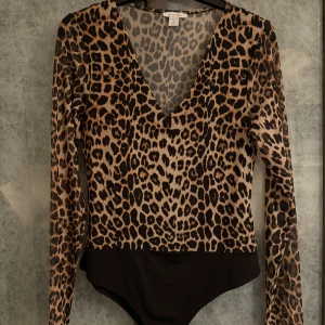 Leopardmönstrad body från Amisu - Säljer en leopardmönstrad body från Amisu i storlek M. Den har en djup v-ringning och långa ärmar. Perfekt för en djärv look! Under ena armhålan har sömmen släppt, se bild. Kan enkelt lagas med några stygn. Annars i mycket fint skick. 
