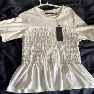 Smock tröja ifrån vero Moda - Säljer en söt vit smock topp från  vero Moda med korta ärmar och smockdetaljer på framsidan. Toppen har en lätt volang nedtill som ger en fin siluett. Perfekt för en stilren look. Köpt för 379kr på Zalando. Aldrig använd! Storlek M