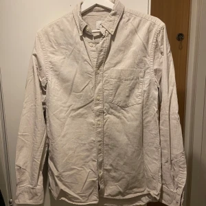 Beige långärmad skjorta - Säljer en stilren beige långärmad skjorta med klassisk krage och bröstficka. Perfekt för en avslappnad men ändå uppklädd look. Skjortan har knappar framtill och är i ett mjukt material.