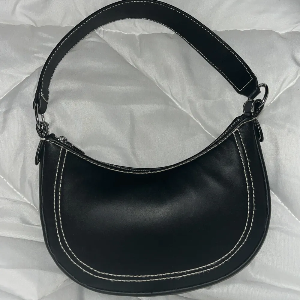 Snygg svart axelväska i skinn med kontrasterande vita sömmar. Väskan har en praktisk dragkedja och en bred axelrem för bekväm användning. Perfekt för att ge en stilren touch till din outfit. Priset går att diskutera.. Laukut & Käsilaukut.