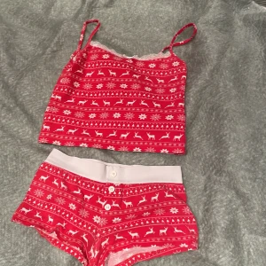 Röd julig linnetopp och shorts från Gina Tricot - Säljer ett rött set med julmönster från Gina Tricot. Linnetoppen har smala axelband och spetsdetaljer vid halsen. Shortsen har en bekväm resår i midjan och knappar framtill. Perfekt för mysiga vinterkvällar! 🎄